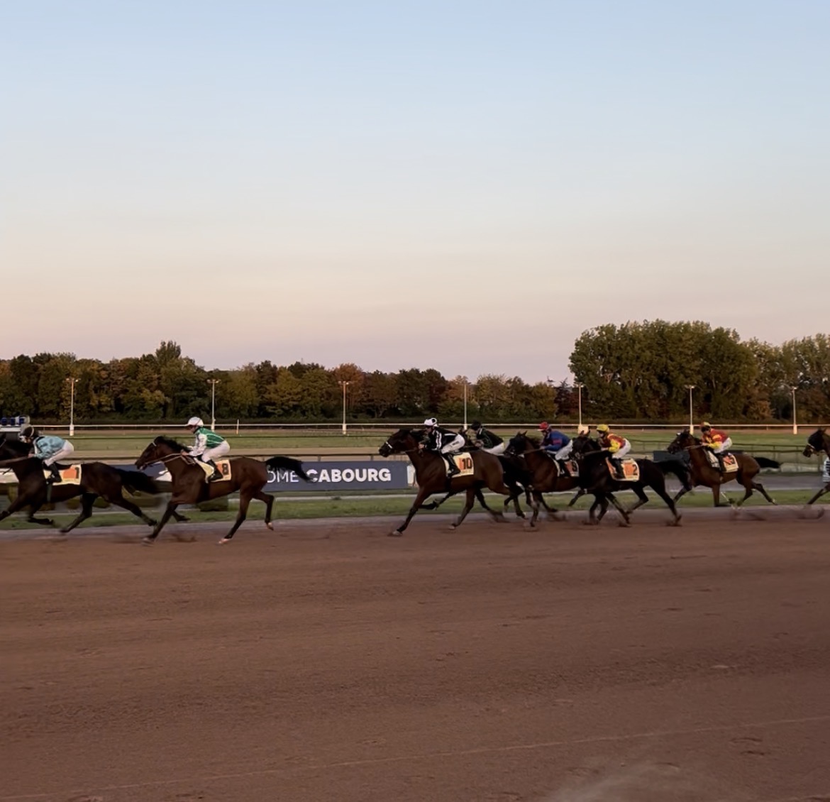 Courses hippiques à l'hippodrome de Cabourg, avec des jockeys et leurs chevaux en pleine course au coucher du soleil